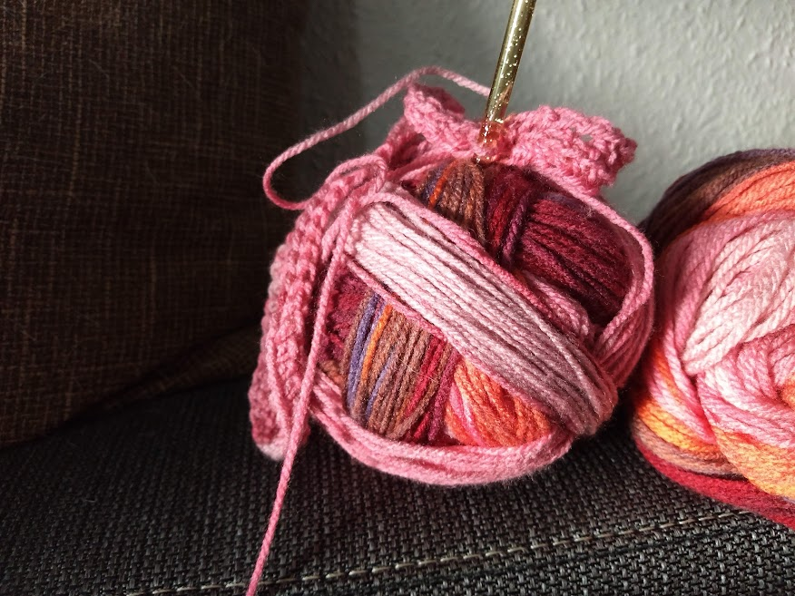 two balls of yarn, one out of focus, the other in the middle of the photo, a started crochet project attached to it with a crochet needle